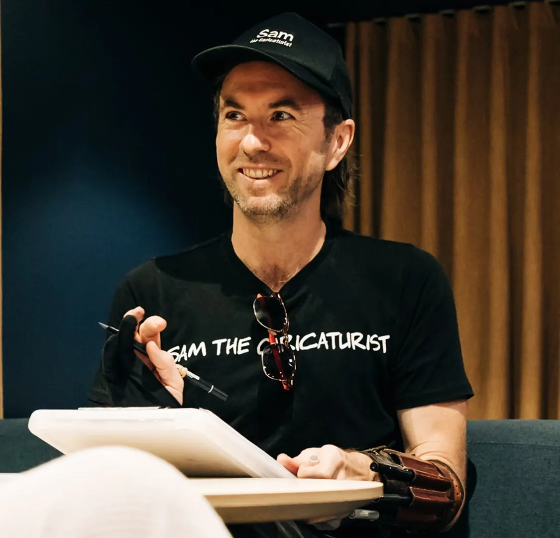 Sam McNair in a black cap drawing on a clipboard and looking up with a smile